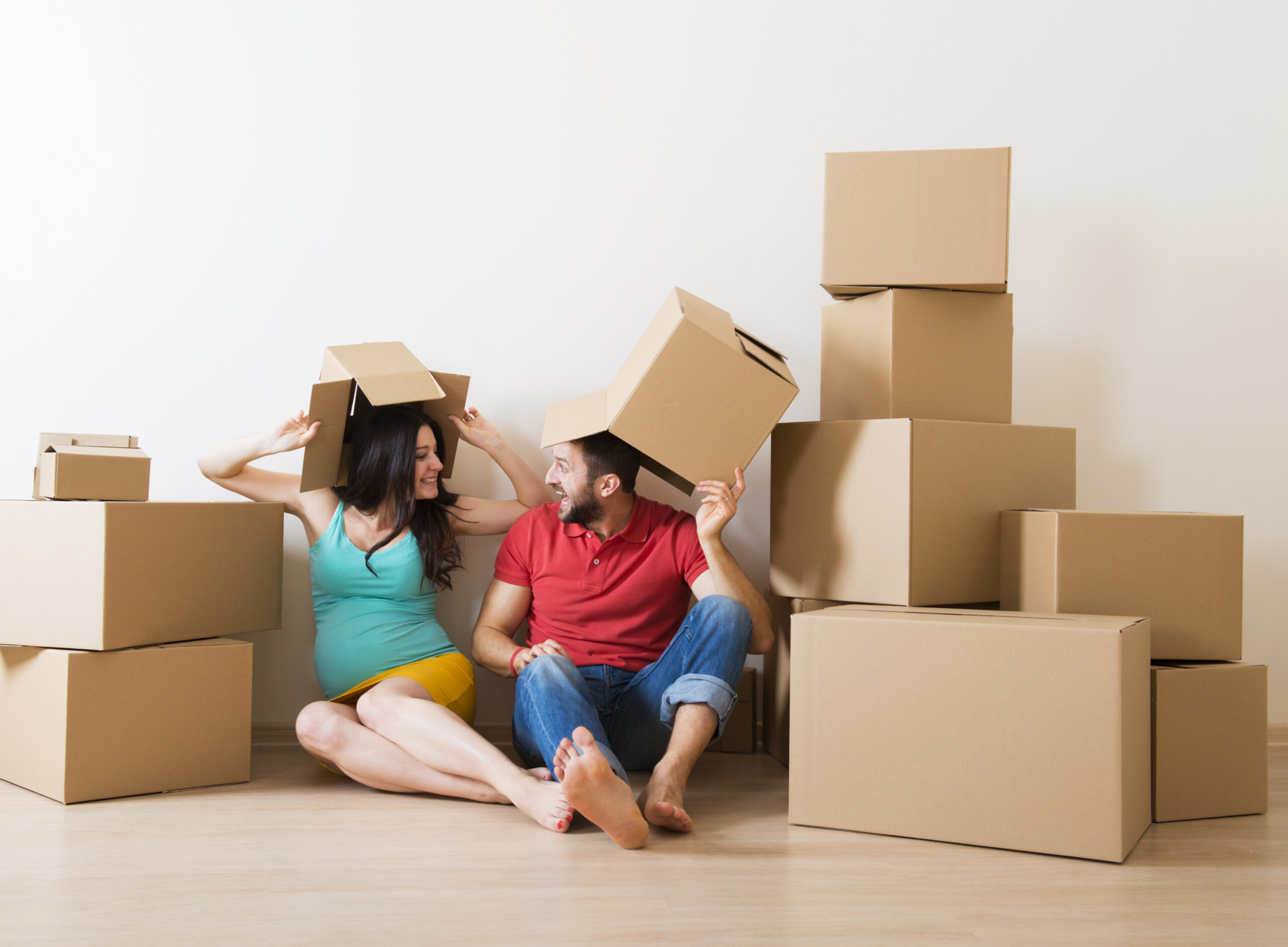 Young couple is moving into new house with lot of boxes. Woman is pregnant.